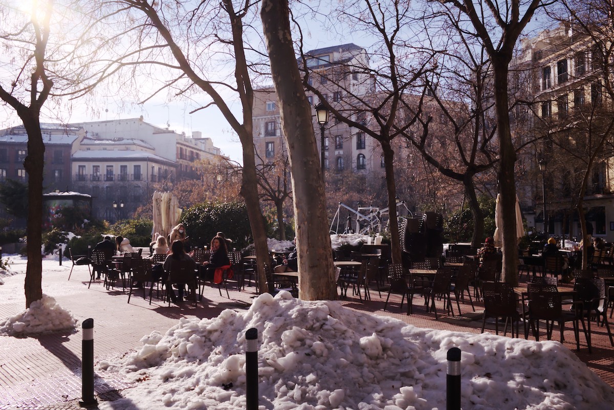 Plaza soleada escondida en Madrid con terraza y algunos montones de nieve.